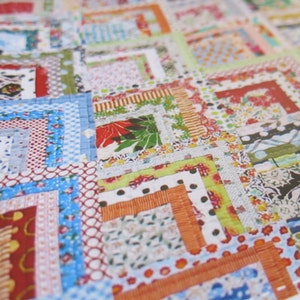 May include: A patchwork quilt with a variety of colorful fabrics and patterns. The quilt is made up of squares and rectangles, and the seams are visible. The quilt is a mix of floral, geometric, and polka dot patterns.