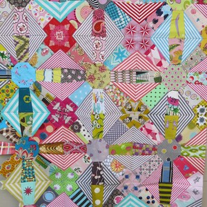 May include: A colourful quilt made of various patterned fabrics in shades of pink, red, blue, green, and yellow. The quilt is made up of squares and diamonds, and the patterns are geometric and floral.