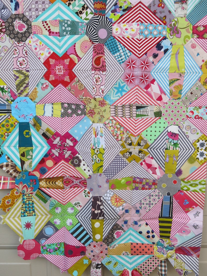 May include: A colourful quilt made of various patterned fabrics in shades of pink, red, blue, green, and yellow. The quilt is made up of squares and diamonds, and the patterns are geometric and floral.