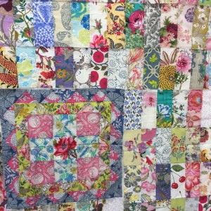 May include: A patchwork quilt with a variety of floral patterns in shades of pink, blue, green, and yellow. The quilt is made up of squares and rectangles of different sizes and is bordered by a dark blue fabric.