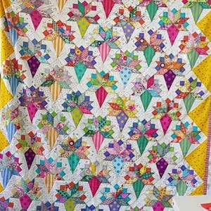 May include: A colorful quilt with a geometric pattern of diamonds and stars. The quilt is made of various fabrics in shades of pink, purple, blue, green, yellow, and white. The quilt is edged with a yellow fabric.