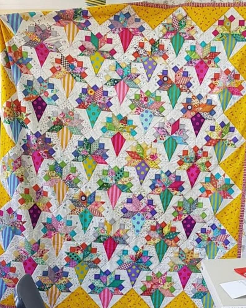 May include: A colorful quilt with a geometric pattern of diamonds and stars. The quilt is made of various fabrics in shades of pink, purple, blue, green, yellow, and white. The quilt is edged with a yellow fabric.