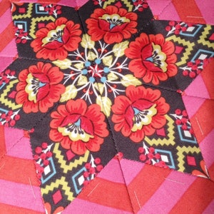 May include: A black fabric star with red and yellow floral designs, surrounded by pink and red striped fabric.