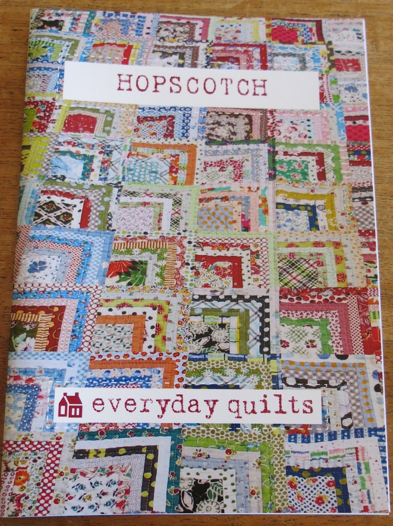 May include: A book cover with a colorful patchwork quilt design. The title "HOPSCOTCH" is printed in white on a white label. The text "everyday quilts" is printed in white on a red label with a small house icon.