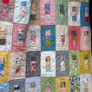 May include: A patchwork quilt featuring a grid of rectangular blocks, each containing smaller multi-coloured fabric squares. The quilt displays a variety of patterns including polka dots, stripes, gingham, and floral prints in shades of red, blue, yellow, green, and pink.
