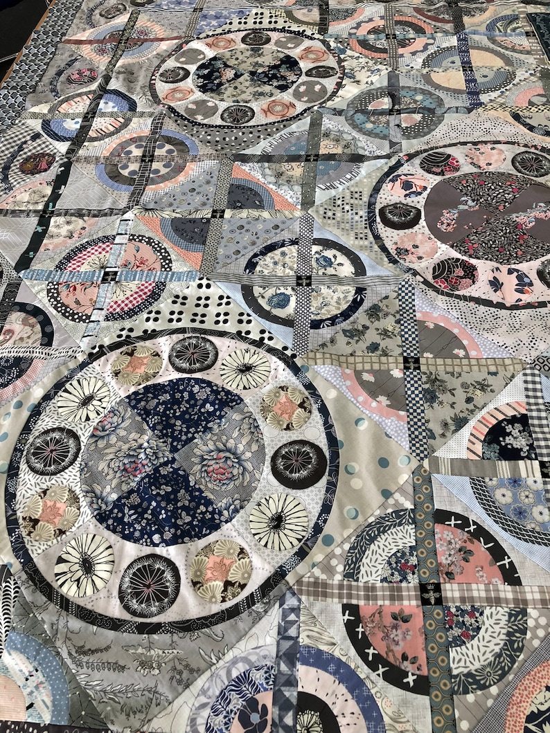 May include: A quilt made of various fabrics in shades of blue, gray, white, and pink. The quilt features a repeating pattern of circles and squares.