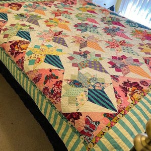 May include: A colorful patchwork quilt with a white background and a variety of floral and geometric patterns. The quilt is made with a variety of fabrics, including cotton and linen. The quilt is edged with a teal and white striped fabric.