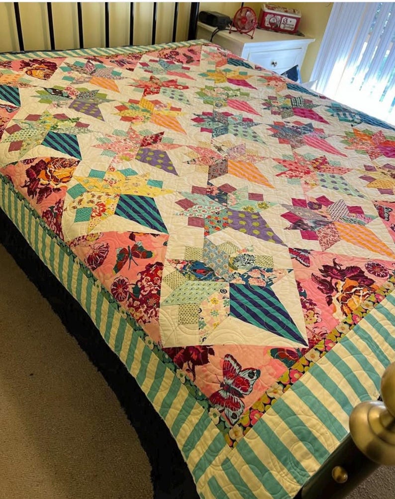 May include: A colorful patchwork quilt with a white background and a variety of floral and geometric patterns. The quilt is made with a variety of fabrics, including cotton and linen. The quilt is edged with a teal and white striped fabric.