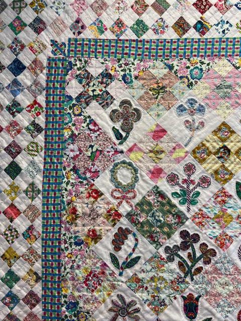 May include: A white quilt with a patchwork design featuring various floral patterns in shades of pink, green, blue, and yellow. The quilt is edged with a blue and green gingham border.