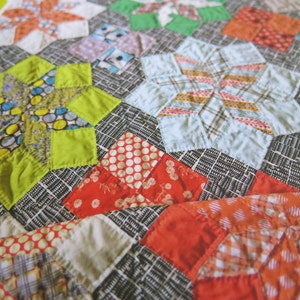 K&ouml;nnte beinhalten: Ein Patchwork-Deckenst&uuml;ck mit einer Vielzahl von bunten Stoffen und Mustern, darunter Sterne, Punkte und Karos. Die Decke ist aus einer Mischung aus hellen und dunklen Stoffen gefertigt, was ein visuell interessantes Design ergibt.
