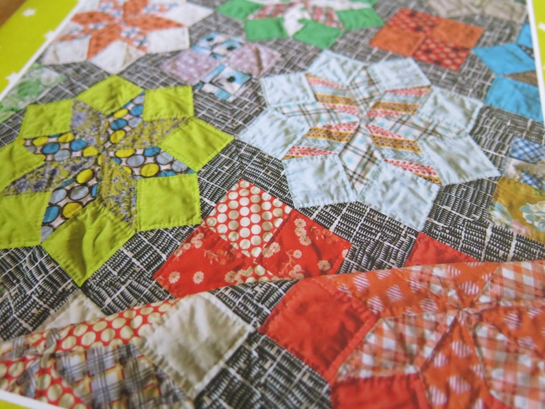 K&ouml;nnte beinhalten: Ein Patchwork-Deckenst&uuml;ck mit einer Vielzahl von bunten Stoffen und Mustern, darunter Sterne, Punkte und Karos. Die Decke ist aus einer Mischung aus hellen und dunklen Stoffen gefertigt, was ein visuell interessantes Design ergibt.