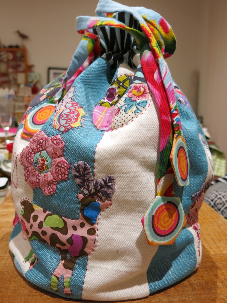 May include: A blue and white drawstring bag with a patchwork design featuring various colorful fabrics, including a pink floral pattern, a brown and white spotted pattern, and a red and yellow swirl pattern.