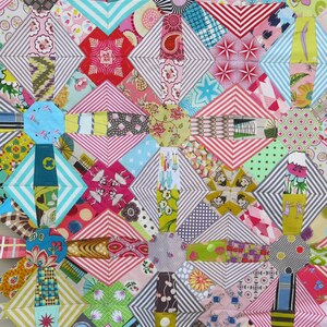 May include: A colourful quilt made of various patterned fabrics. The quilt is made up of a variety of geometric shapes, including squares, triangles, and diamonds. The quilt is a mix of bright colours, including red, pink, blue, green, and yellow.