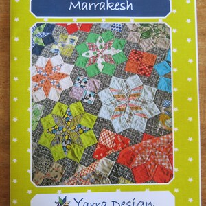 K&ouml;nnte beinhalten: Ein gr&uuml;nes, gelbes und rotes Quiltmuster mit dem Titel "Marrakesh" und dem Text "Yarra Design" auf gelbem Hintergrund mit wei&szlig;en Sternen.