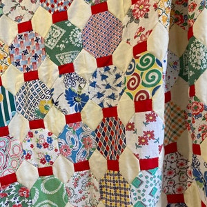 Peut inclure: Une courtepointe en patchwork avec un motif hexagonal. La courtepointe est faite de différents tissus avec des motifs floraux, géométriques et abstraits. La courtepointe est principalement blanche avec des accents rouges.