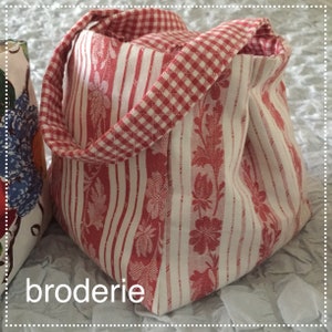 May include: A red and white striped fabric tote bag with a gingham handle. The bag has a floral pattern and the word "broderie" is printed on the bottom.