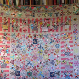 May include: A colorful patchwork quilt with a floral theme. The quilt is made up of various fabrics in shades of pink, red, blue, green, and yellow. The quilt is decorated with a variety of floral motifs, including flowers, leaves, and stems. The quilt is displayed on a wall.