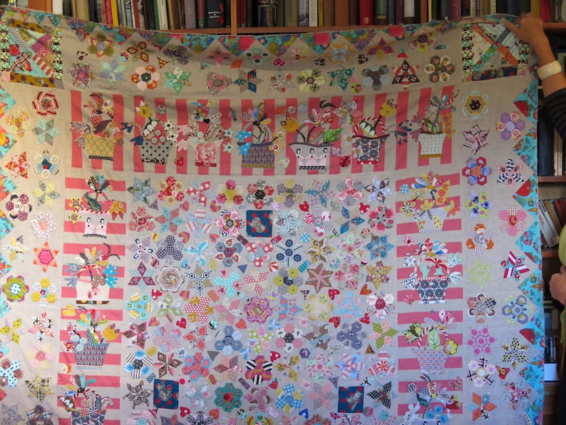 May include: A colorful patchwork quilt with a floral theme. The quilt is made up of various fabrics in shades of pink, red, blue, green, and yellow. The quilt is decorated with a variety of floral motifs, including flowers, leaves, and stems. The quilt is displayed on a wall.