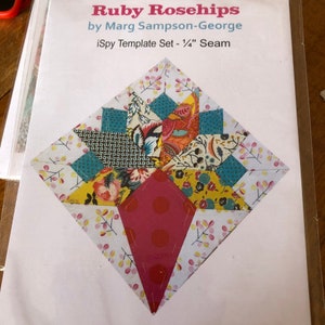 Puede incluir: Un patrón de bloque de colcha llamado "Ruby Rosehips" de Marg Sampson-George. El patrón es para un conjunto de plantillas iSpy con una tolerancia de costura de 1/4 de pulgada. El bloque está hecho de recortes de tela coloridos con patrones florales y geométricos.