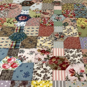 K&ouml;nnte beinhalten: Ein Patchwork-Deckenst&uuml;ck mit einer Vielzahl von floralen und geometrischen Mustern in Rosa-, Blau-, Gr&uuml;n- und Braunt&ouml;nen. Die Decke besteht aus vielen kleinen Quadraten und Sechsecken, die ein komplexes und interessantes Design ergeben.