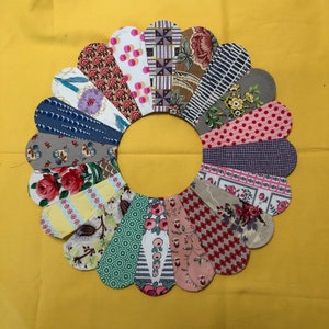 May include: A colorful patchwork quilt block in the shape of a flower with 16 petals. Each petal is made from a different fabric with a variety of patterns and colors, including red, pink, blue, green, yellow, and brown.
