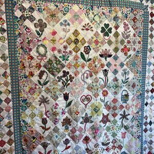 May include: A white quilt with a diamond pattern. Each diamond is filled with a different fabric featuring a variety of floral designs. The quilt is bordered with a blue and green patterned fabric.