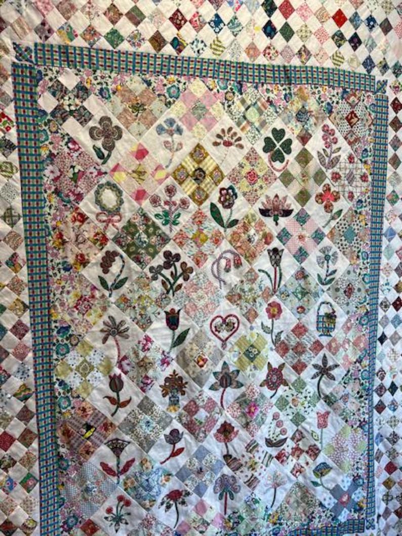 May include: A white quilt with a diamond pattern. Each diamond is filled with a different fabric featuring a variety of floral designs. The quilt is bordered with a blue and green patterned fabric.