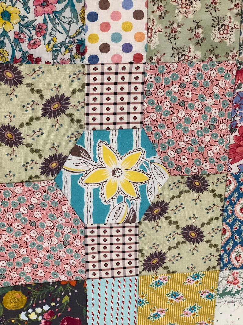 K&ouml;nnte beinhalten: Ein Patchwork-Deckenst&uuml;ck mit verschiedenen floralen und geometrischen Mustern in den Farben Rosa, Blau, Gr&uuml;n, Gelb und Braun.