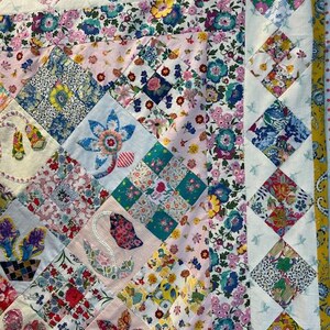 May include: A patchwork quilt with a floral pattern in shades of pink, blue, and yellow. The quilt is made up of squares of different fabrics, each with a unique design. The quilt is edged with a white border and a blue and white diamond pattern.