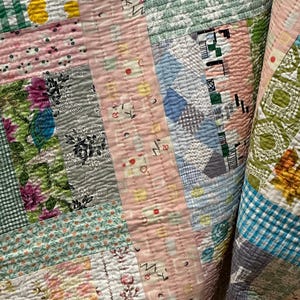 Puede incluir: Una colcha de retazos con una variedad de patrones florales y geom&eacute;tricos en tonos de rosa, azul, verde y blanco. La colcha est&aacute; hecha de diferentes telas y texturas, creando un dise&ntilde;o &uacute;nico e interesante.