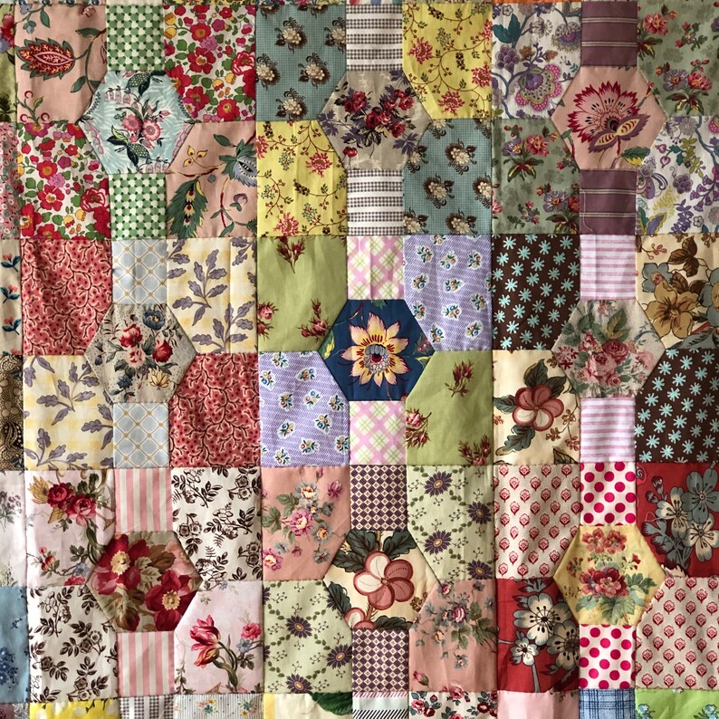 Puede incluir: Una colcha de retazos con un patr&oacute;n hexagonal. La colcha est&aacute; hecha de varias telas con estampados florales en tonos de rosa, azul, verde y marr&oacute;n.