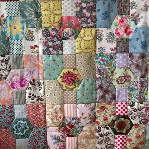 Puede incluir: Una colcha de retazos con una variedad de patrones florales en tonos de rosa, azul, verde y blanco. La colcha est&aacute; hecha de formas hexagonales y est&aacute; cosida con hilo blanco.