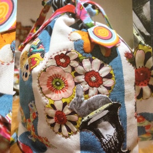 May include: A white fabric bag with a drawstring closure. The bag is decorated with colorful fabric scraps, including flowers, a rabbit, and a cup. The bag is made of a patchwork of different fabrics.