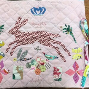 May include: A pink quilted fabric project bag with a brown rabbit, dragonfly, and bird appliques. The bag has a crown applique and the text "Projects 2017". The bag has two fabric ties.