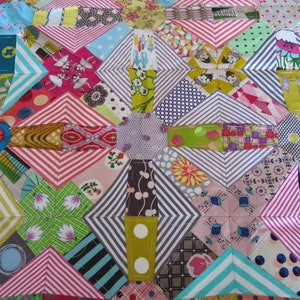 May include: A colourful patchwork quilt with a geometric pattern. The quilt is made up of various fabrics in shades of pink, green, blue, and white. The quilt is stitched together with a white thread.