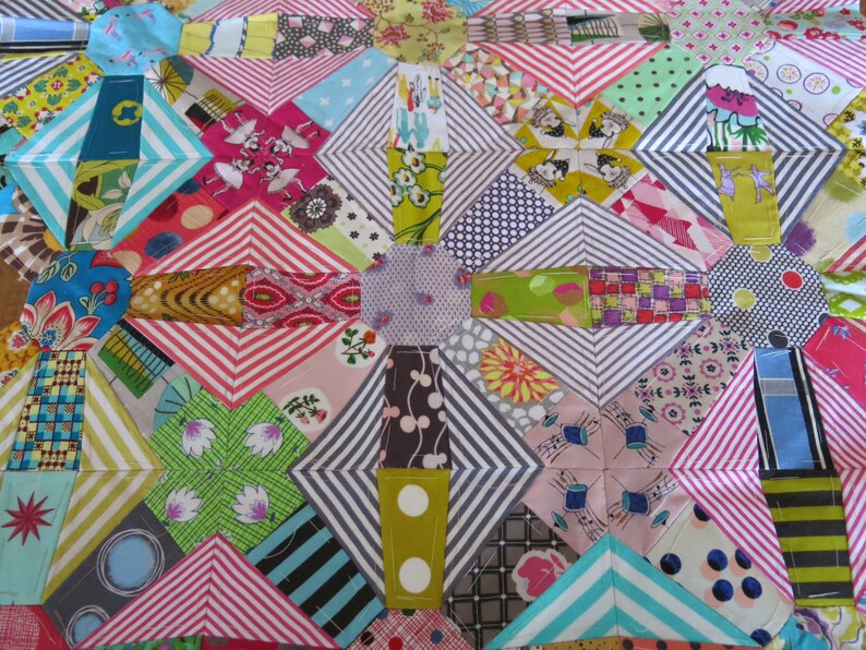 May include: A colourful patchwork quilt with a geometric pattern. The quilt is made up of various fabrics in shades of pink, green, blue, and white. The quilt is stitched together with a white thread.