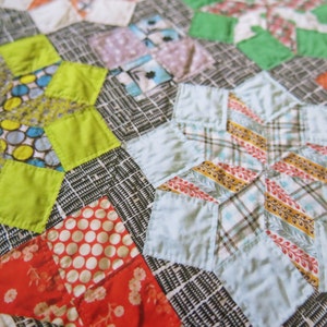 K&ouml;nnte beinhalten: Ein Patchwork-Deckenst&uuml;ck mit einer Vielzahl von bunten Stoffen, darunter Gr&uuml;n, Blau, Gelb, Rot und Wei&szlig;. Die Decke besteht aus verschiedenen Formen, darunter Sterne, Quadrate und Rauten.