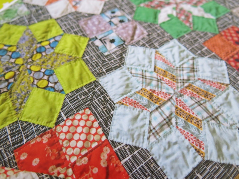 K&ouml;nnte beinhalten: Ein Patchwork-Deckenst&uuml;ck mit einer Vielzahl von bunten Stoffen, darunter Gr&uuml;n, Blau, Gelb, Rot und Wei&szlig;. Die Decke besteht aus verschiedenen Formen, darunter Sterne, Quadrate und Rauten.