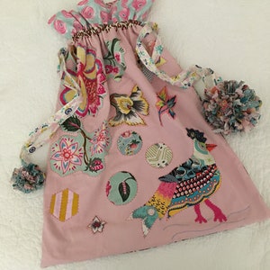 May include: A pink fabric bag with a drawstring closure. The bag is decorated with colorful floral and bird appliques. The bag has a whimsical and handmade aesthetic.