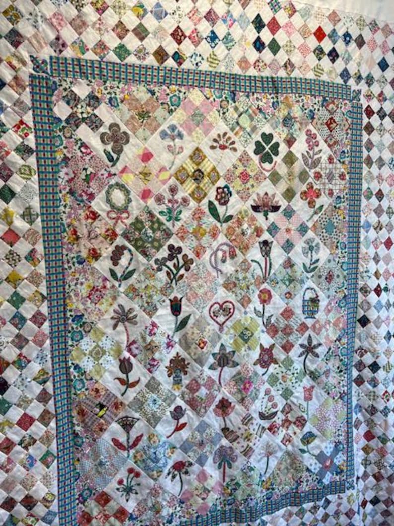 May include: A white quilt with a patchwork design featuring various floral patterns and colors. The quilt is bordered with a blue and white checkered fabric.