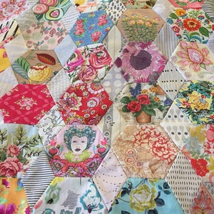 Könnte beinhalten: Eine Patchwork-Decke mit einem sechseckigen Muster. Die Decke besteht aus verschiedenen Stoffen mit Blumendrucken in den Farben Rosa, Rot, Blau, Grün und Gelb. Die Decke ist eine Mischung aus verschiedenen Mustern und Texturen.