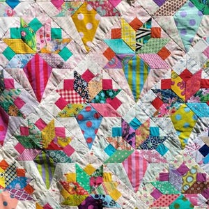 May include: A colorful patchwork quilt with a variety of fabrics and patterns. The quilt is made up of squares and triangles, and the colors are bright and cheerful.