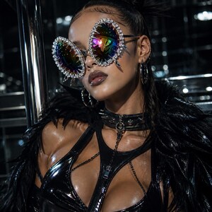 May include: A person wearing large, iridescent sunglasses with a gold frame and crystal embellishments. They are also wearing a black leather top with a zipper, a choker, and a black feather boa.