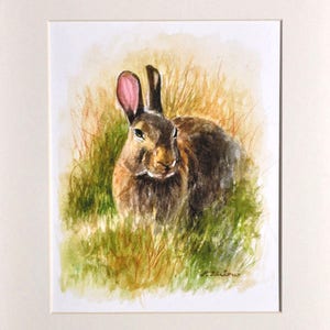 May include: Watercolor painting of a brown rabbit with pink ears sitting in a field of green grass.