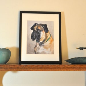 May include: A framed painting of a brown and black dog with a green collar. The painting is on a wooden shelf with a teal ceramic bowl and a bronze swan figurine.