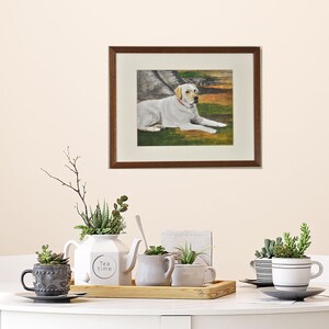 May include: A framed painting of a white Labrador Retriever lying down in a grassy field. The dog is wearing a red collar and looking to the right. The painting is in a brown frame with a white mat.