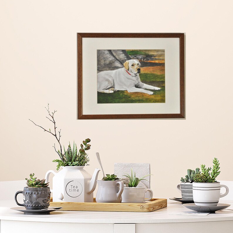 May include: A framed painting of a white Labrador Retriever lying down in a grassy field. The dog is wearing a red collar and looking to the right. The painting is in a brown frame with a white mat.