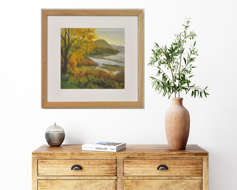 Puede incluir: Una pintura enmarcada de una escena de paisaje con un r&iacute;o serpenteando a trav&eacute;s de un valle. Los &aacute;rboles est&aacute;n en colores oto&ntilde;ales de amarillo, naranja y rojo. El cielo es de un azul suave con nubes.