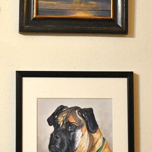 May include: A framed painting of a dog, a Bullmastiff, with a green collar. The dog is looking to the left of the image. The painting is in a black frame with a white mat.