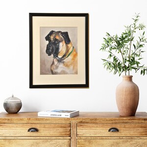 May include: A framed painting of a brown and black dog with a green collar. The dog is looking to the left of the frame. The painting is in a black frame and is hanging on a white wall.